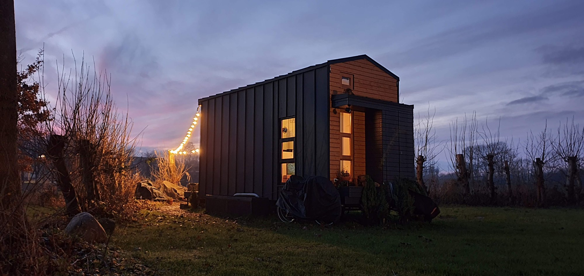Tiny House Tiny Escape in der Abenddämmerung mit Lichterkette in Delve
